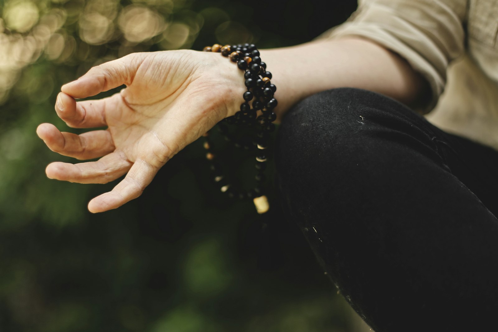 A hand resting on the knee holding mala prayer beads